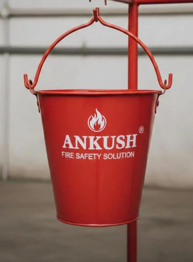 Red steel fire bucket with stand manufactured by Ankush Fire Safety Solutions, displaying a durable fire bucket used for fire safety in industrial and commercial environments